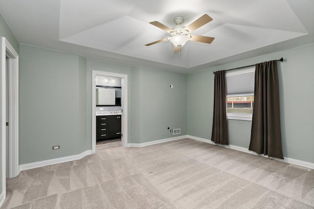 unfurnished bedroom featuring ceiling fan, light carpet, a tray ceiling, and ensuite bath