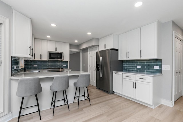 kitchen featuring white cabinetry, sink, stainless steel appliances, kitchen peninsula, and a kitchen bar