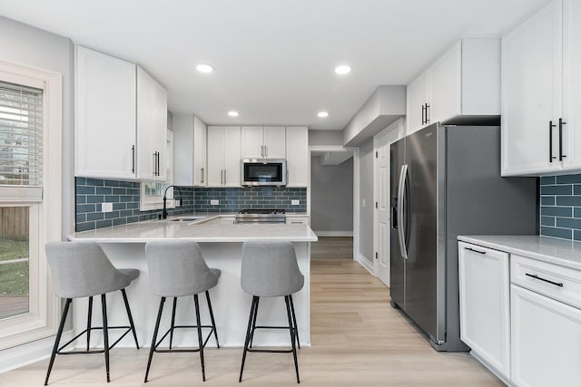 kitchen with appliances with stainless steel finishes, light wood-type flooring, a breakfast bar, sink, and white cabinets