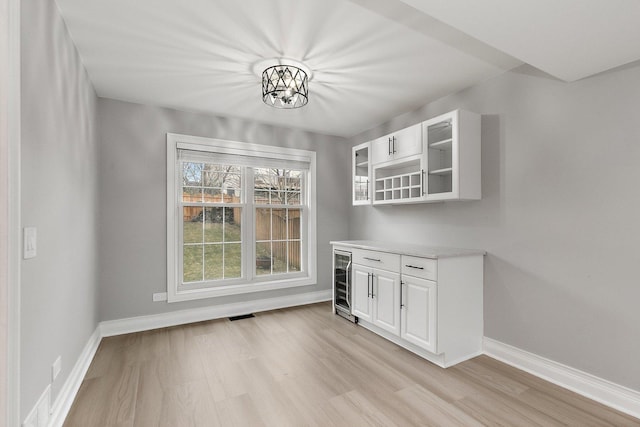 unfurnished dining area featuring light wood-type flooring, wine cooler, and a chandelier