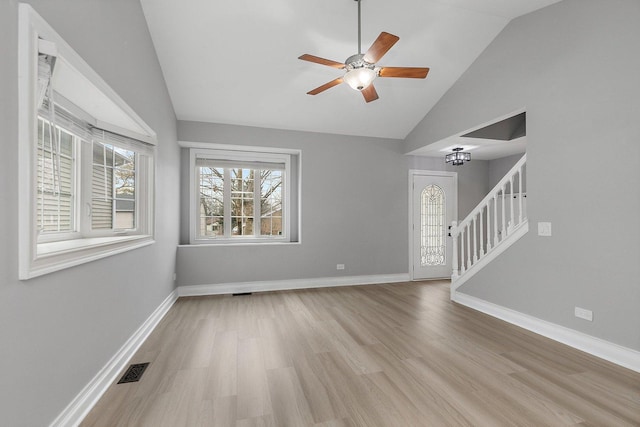 unfurnished living room featuring ceiling fan with notable chandelier, vaulted ceiling, and light wood-type flooring