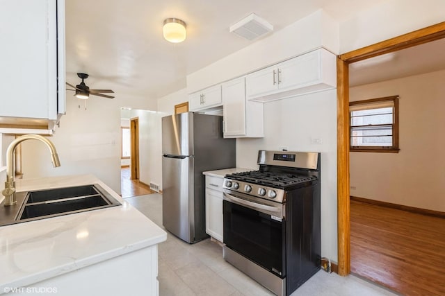 kitchen featuring baseboards, white cabinets, a ceiling fan, appliances with stainless steel finishes, and a sink