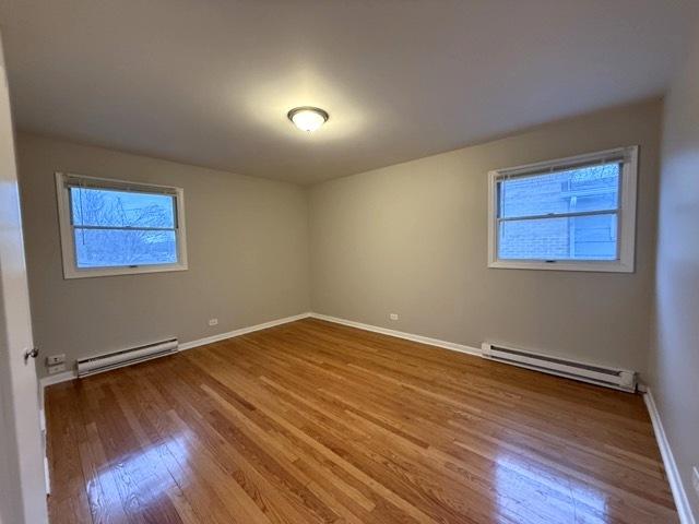 spare room featuring hardwood / wood-style floors, plenty of natural light, and a baseboard heating unit