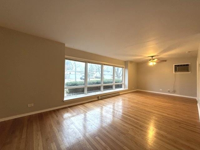 empty room featuring wood-type flooring, a baseboard radiator, a wall mounted AC, and ceiling fan