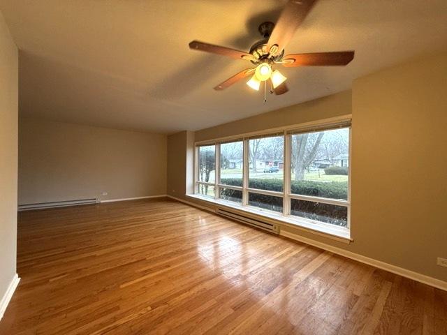 spare room with ceiling fan, hardwood / wood-style floors, and a baseboard heating unit