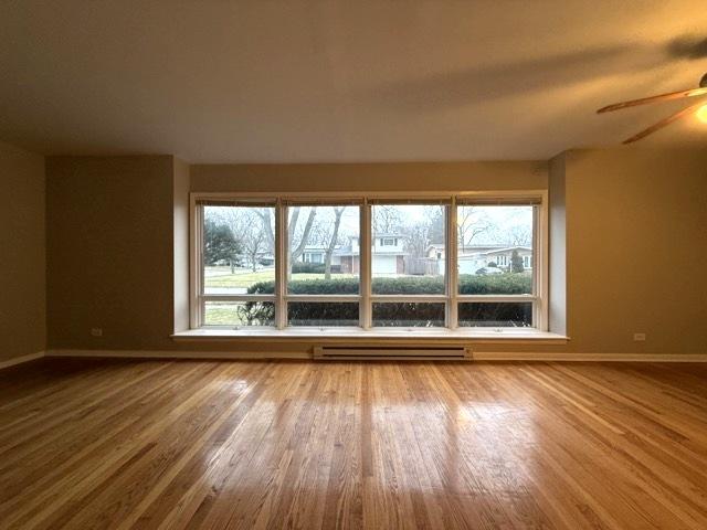 empty room featuring ceiling fan, hardwood / wood-style floors, and a baseboard heating unit