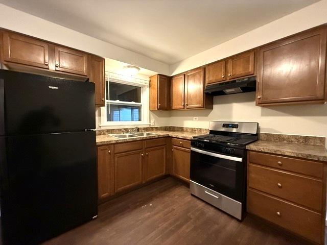 kitchen with gas range, black fridge, dark wood-type flooring, and sink