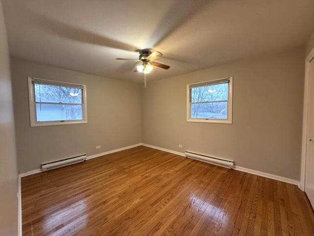 empty room featuring hardwood / wood-style floors, plenty of natural light, and baseboard heating