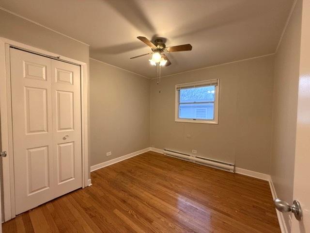 unfurnished bedroom with hardwood / wood-style floors, a closet, baseboard heating, and ceiling fan