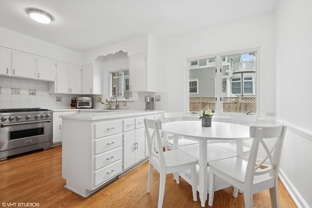 kitchen featuring white cabinetry, backsplash, stainless steel stove, and light hardwood / wood-style floors