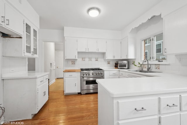 kitchen featuring high end stove, sink, white cabinets, kitchen peninsula, and light hardwood / wood-style flooring