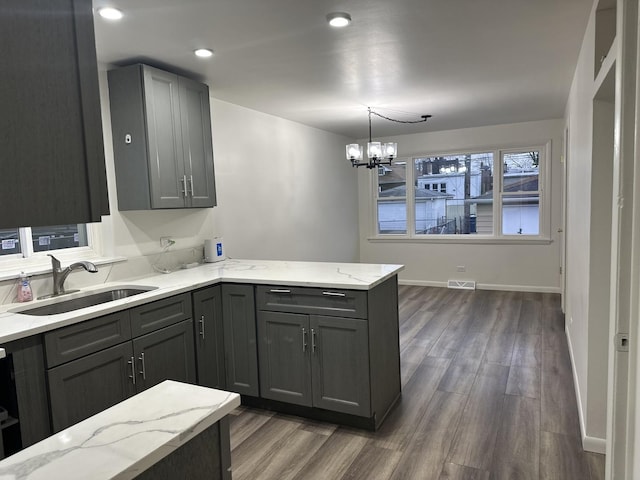 kitchen featuring gray cabinetry, sink, light stone counters, pendant lighting, and a chandelier