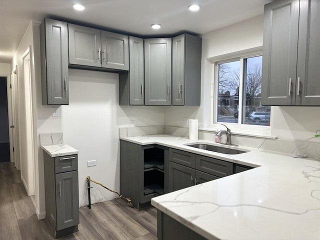 kitchen with light stone countertops, gray cabinets, dark wood-type flooring, and sink