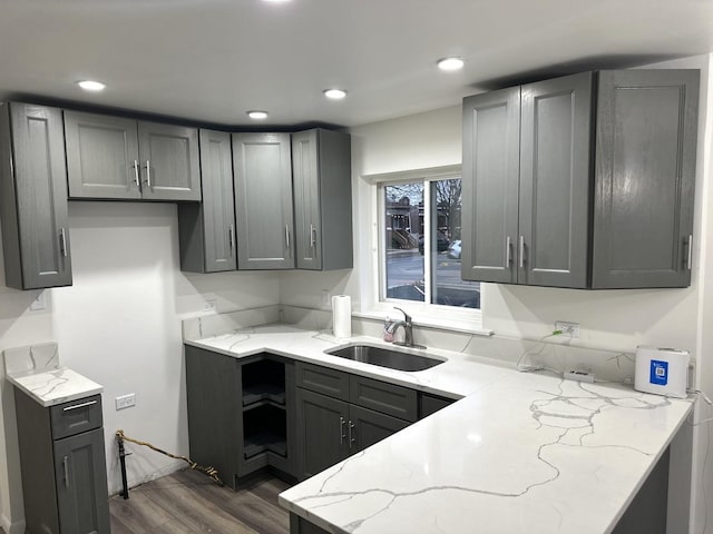 kitchen with gray cabinetry, dark hardwood / wood-style floors, light stone countertops, and sink