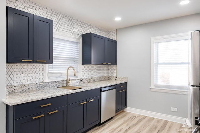 kitchen with sink, appliances with stainless steel finishes, light stone counters, light hardwood / wood-style floors, and decorative backsplash