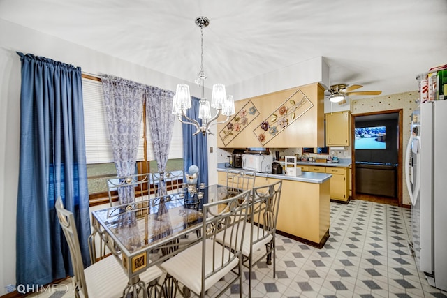 kitchen with kitchen peninsula, pendant lighting, white appliances, light brown cabinetry, and ceiling fan with notable chandelier