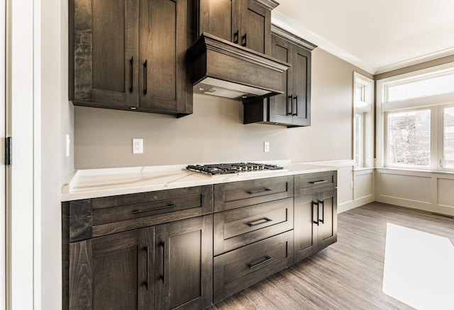 kitchen featuring light wood-type flooring, light stone counters, ornamental molding, dark brown cabinets, and stainless steel gas cooktop