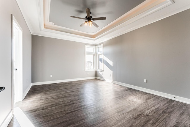 empty room featuring a raised ceiling, ceiling fan, dark hardwood / wood-style flooring, and ornamental molding