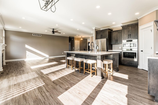 kitchen featuring a kitchen breakfast bar, stainless steel appliances, ceiling fan, dark wood-type flooring, and a center island with sink