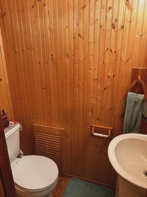 bathroom featuring toilet, sink, and wooden walls