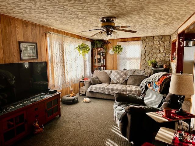 living room with carpet flooring, ceiling fan, and wooden walls