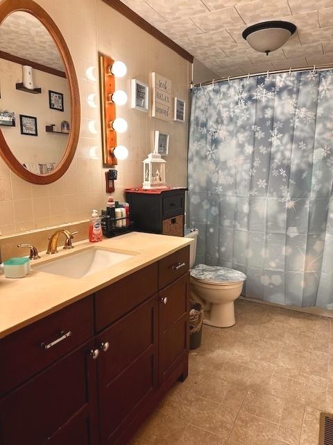 bathroom with vanity, toilet, crown molding, and tile walls