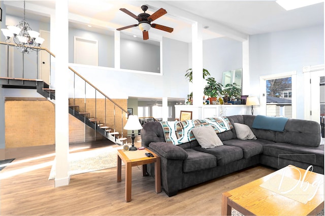 living room featuring light hardwood / wood-style flooring, a towering ceiling, and ceiling fan with notable chandelier