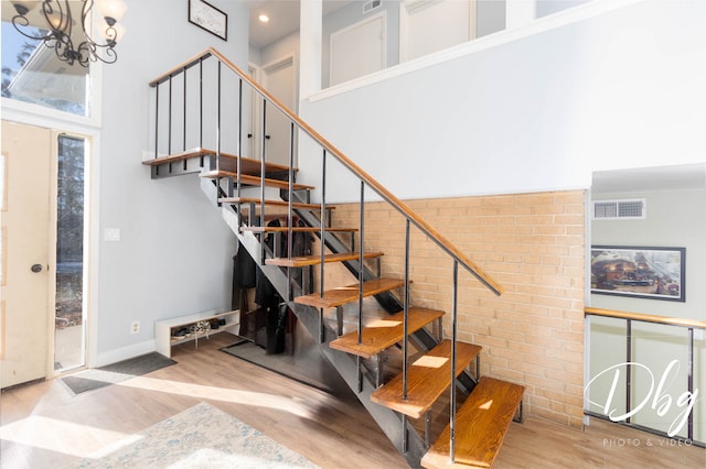 stairway with a towering ceiling, hardwood / wood-style flooring, and an inviting chandelier