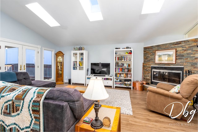 living room with light hardwood / wood-style flooring, french doors, a stone fireplace, and lofted ceiling with skylight