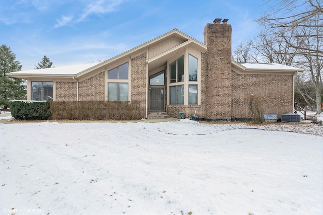 snow covered rear of property featuring central AC unit