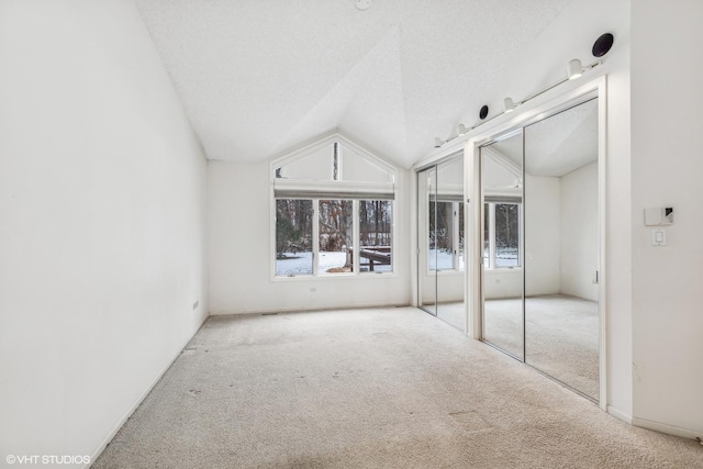 unfurnished bedroom featuring a textured ceiling, two closets, vaulted ceiling, and light colored carpet