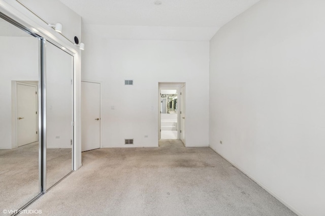 unfurnished bedroom with light carpet, high vaulted ceiling, and a closet