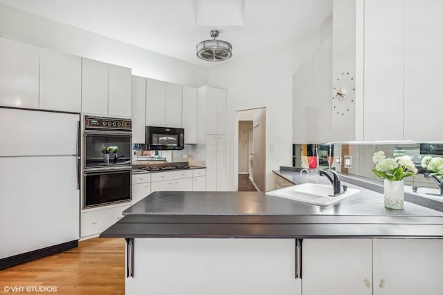 kitchen with white cabinetry, sink, kitchen peninsula, black appliances, and light wood-type flooring