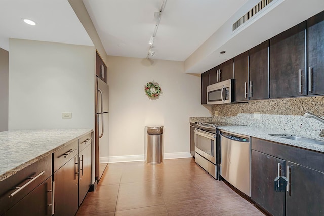 kitchen with sink, light stone countertops, rail lighting, and appliances with stainless steel finishes