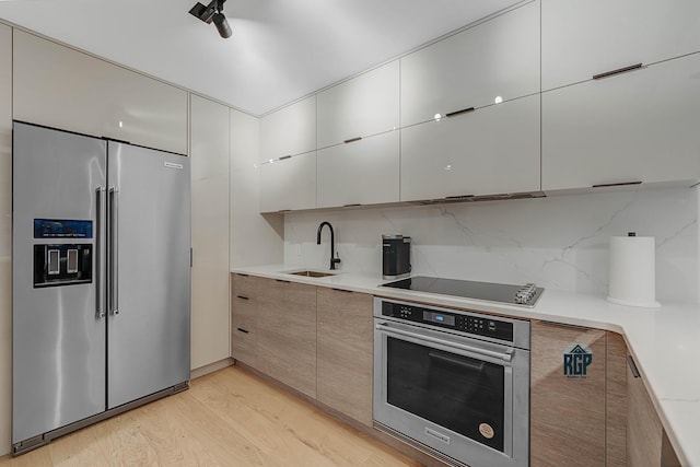 kitchen with backsplash, sink, stainless steel appliances, and light hardwood / wood-style flooring