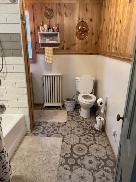 bathroom featuring radiator heating unit, tile patterned floors, wood walls, shower / bath combination with curtain, and toilet