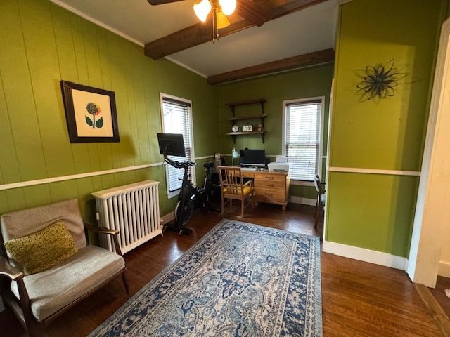 home office featuring beamed ceiling, a wealth of natural light, dark wood-type flooring, and radiator