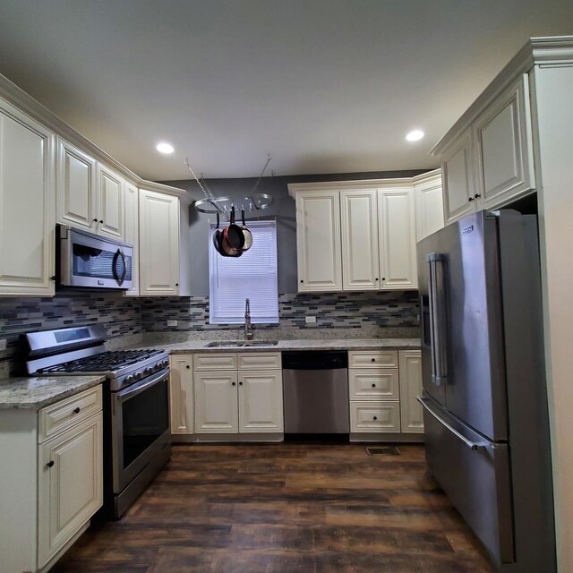 kitchen with sink, dark hardwood / wood-style floors, appliances with stainless steel finishes, tasteful backsplash, and light stone counters