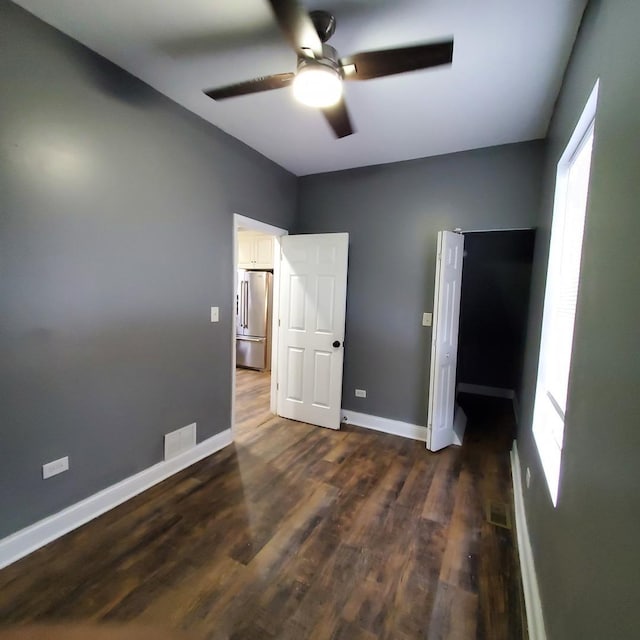 unfurnished bedroom with ceiling fan, stainless steel fridge, and dark hardwood / wood-style floors