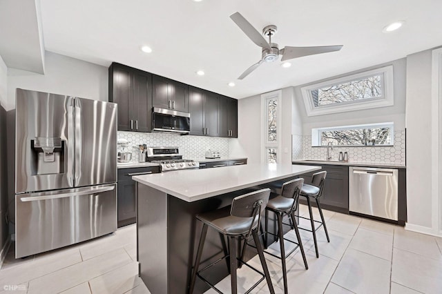 kitchen featuring light tile patterned floors, a breakfast bar area, ceiling fan, stainless steel appliances, and a kitchen island