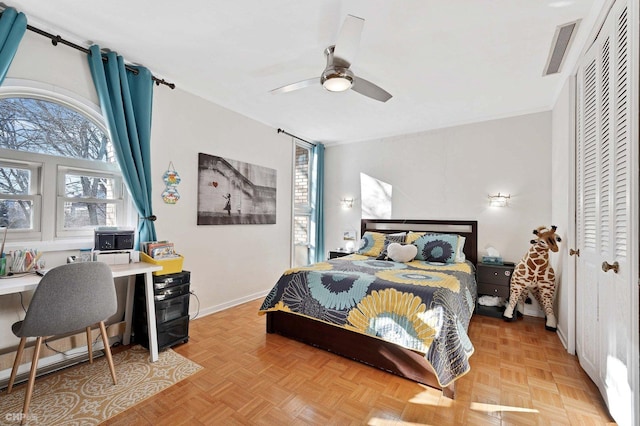 bedroom featuring multiple windows, light parquet flooring, ceiling fan, and a closet