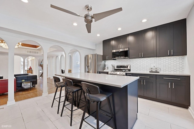 kitchen with light tile patterned flooring, a kitchen bar, a kitchen island, ceiling fan, and stainless steel appliances