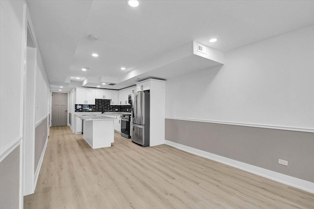 kitchen featuring a center island, light hardwood / wood-style flooring, decorative backsplash, appliances with stainless steel finishes, and white cabinetry