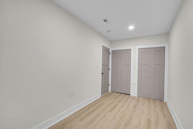 unfurnished bedroom featuring multiple closets and light hardwood / wood-style floors