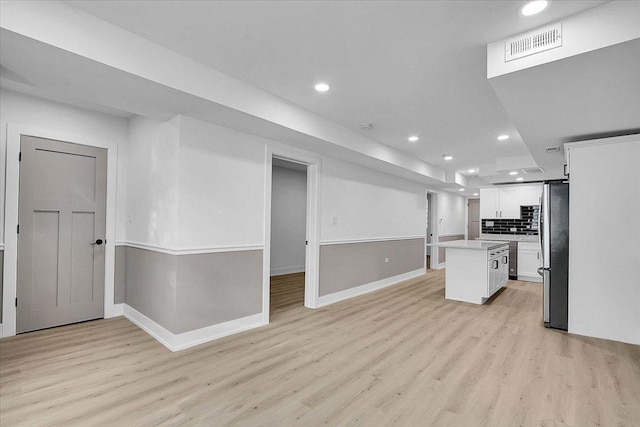 kitchen with stainless steel refrigerator, white cabinetry, a center island, light hardwood / wood-style flooring, and backsplash