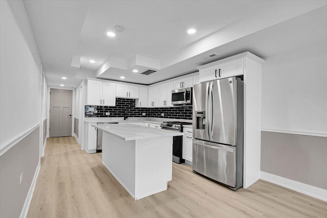 kitchen with white cabinets, light hardwood / wood-style floors, appliances with stainless steel finishes, a kitchen island, and light stone counters