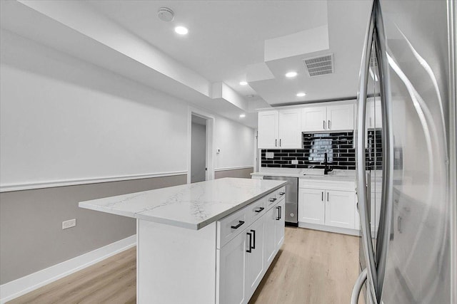 kitchen featuring light stone countertops, stainless steel appliances, a kitchen island, and white cabinetry