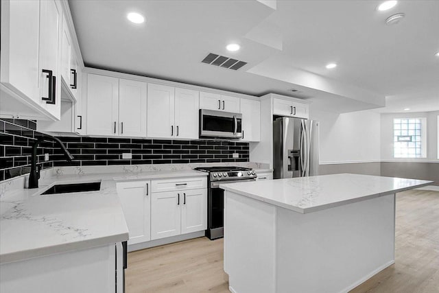 kitchen featuring white cabinets, sink, a kitchen island, light stone counters, and stainless steel appliances