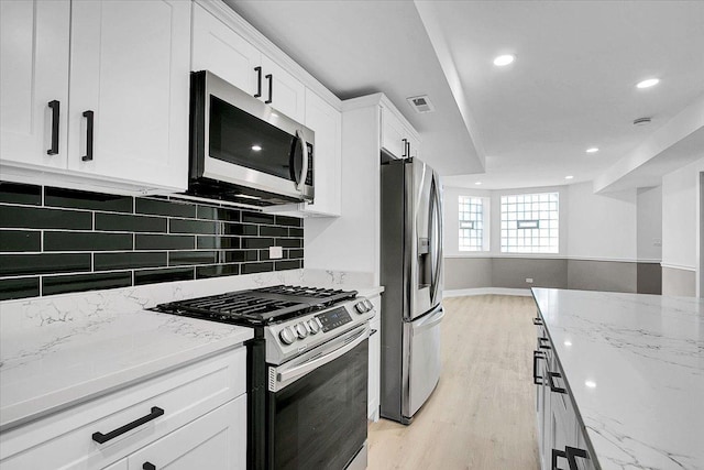 kitchen with stainless steel appliances, light stone counters, light hardwood / wood-style floors, decorative backsplash, and white cabinets