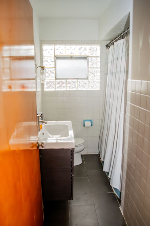 bathroom with tile patterned flooring, vanity, toilet, and tile walls